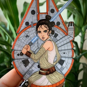 Puede incluir: Una ilustración dibujada a mano de Rey de Star Wars sosteniendo un sable de luz frente a un Halcón Milenario. La ilustración está en un estilo de dibujos animados y presenta un fondo blanco.