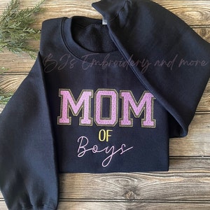 May include: Black sweatshirt with pink and gold embroidery that reads "MOM OF BOYS".