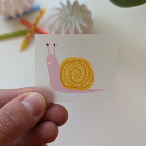 Könnte beinhalten: Eine rosa Schnecke mit einer gelben Schale mit weißen Punkten. Die Schnecke lächelt.