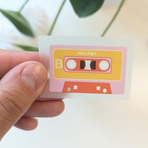Könnte beinhalten: Ein rosa und gelber Kassetten-Aufkleber mit dem Text "mix tape" darauf.