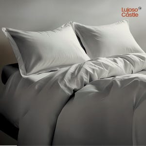 May include: A bed with white bedding, featuring two white pillowcases with a border and a white duvet cover. The bedding is arranged to create a neat appearance. The brand name "Lujoso Castle" is visible in the top right corner of the image.
