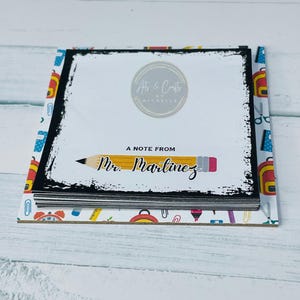 Könnte beinhalten: Ein Notizblock mit schwarzem Rand und Bleistiftmuster. Der Notizblock trägt den Text "A Note From Mr. Martinez" und das Logo "Arts & Crafts by Michelle". Der Notizblock ist von einem gemusterten Rand mit Schulmaterialien umgeben.