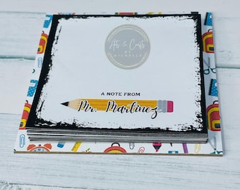 May include: A stack of notepads with a black border and a pencil design. The notepad has the text "A Note From Mr. Martinez" and the logo "Arts & Crafts by Michelle". The notepad is surrounded by a patterned border with school supplies.