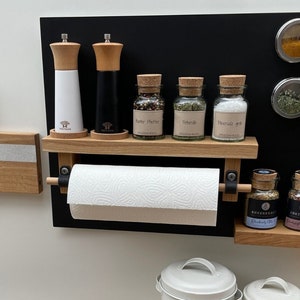 Könnte beinhalten: Ein Küchenorganizer aus Holz mit einem magnetischen Gewürzregal, einem Papierhandtuchhalter und einem Messerhalter. Der Organizer ist an einer weißen Wand montiert. Es gibt auch zwei Metallbehälter mit den Aufschriften "Zwiebeln" und "Knoblauch".