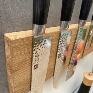 Peut inclure: Un porte-couteaux magn&eacute;tique en bois avec cinq couteaux argent&eacute;s &agrave; manches noirs. Les couteaux ont une finition martel&eacute;e et la marque "XINZUO" est visible sur l'un des couteaux.