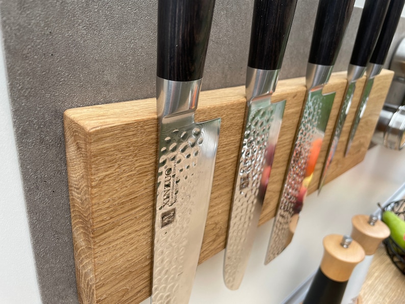 Peut inclure: Un porte-couteaux magn&eacute;tique en bois avec cinq couteaux argent&eacute;s &agrave; manches noirs. Les couteaux ont une finition martel&eacute;e et la marque "XINZUO" est visible sur l'un des couteaux.