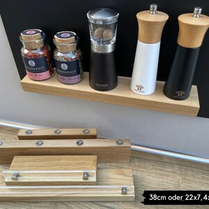 Puede incluir: Un juego de estantes magn&eacute;ticos para especias de madera con cuatro tarros de especias de vidrio y tres molinillos de pimienta de metal. Los tarros de especias est&aacute;n etiquetados como "Chili Powder" y "Greek Herbs". Los molinillos de pimienta son negros, blancos y de madera. Los estantes est&aacute;n montados en una pizarra negra.
