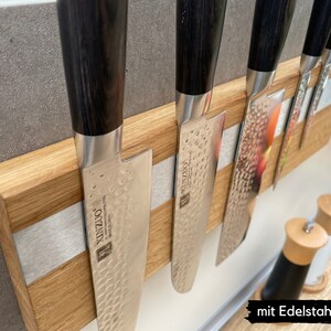 Peut inclure: Un porte-couteaux magn&eacute;tique en bois avec une bande argent&eacute;e et cinq couteaux &agrave; manches noirs. Les couteaux ont une finition martel&eacute;e et le texte "KINZU" est visible sur la lame.
