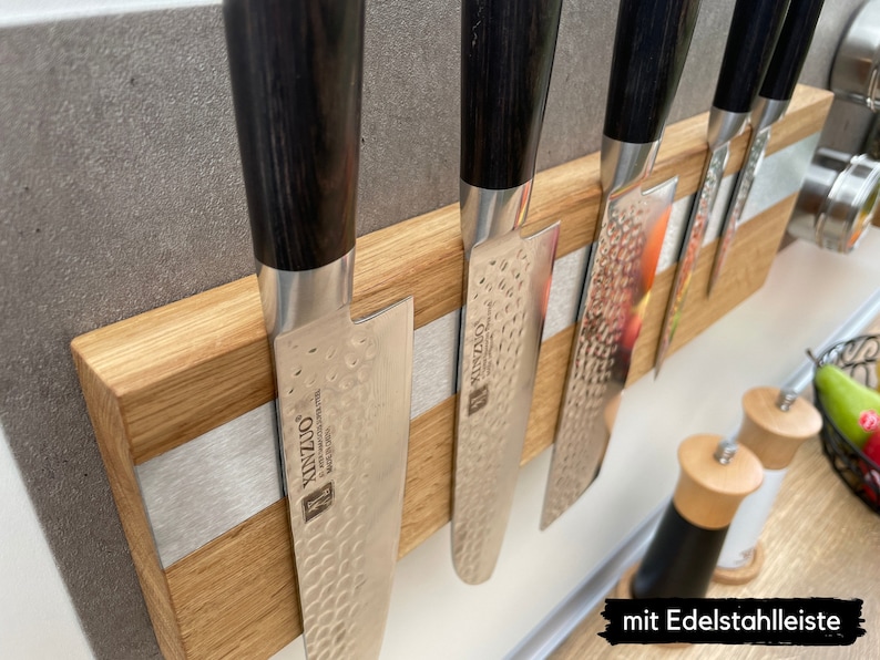 Peut inclure: Un porte-couteaux magn&eacute;tique en bois avec une bande argent&eacute;e et cinq couteaux &agrave; manches noirs. Les couteaux ont une finition martel&eacute;e et le texte "KINZU" est visible sur la lame.
