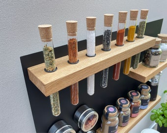 Peut inclure: Un présentoir à épices en bois avec des tubes en verre et des bouchons en liège, remplis de diverses épices. Le présentoir comprend également de petits bocaux en verre avec des épices et un fond noir.