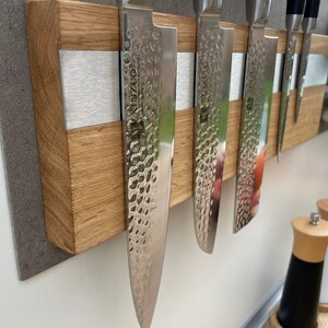 Peut inclure: Un porte-couteaux magn&eacute;tique en bois avec une bande argent&eacute;e au centre. Cinq couteaux argent&eacute;s sont fix&eacute;s au porte-couteaux. Le porte-couteaux est mont&eacute; sur un mur gris.