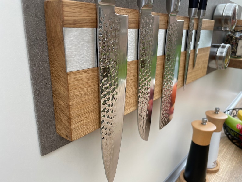 Peut inclure: Un porte-couteaux magn&eacute;tique en bois avec une bande argent&eacute;e au centre. Cinq couteaux argent&eacute;s sont fix&eacute;s au porte-couteaux. Le porte-couteaux est mont&eacute; sur un mur gris.