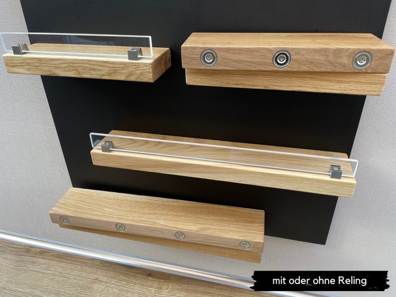 Puede incluir: Tres estantes de madera con cierres magn&eacute;ticos de metal. El estante superior tiene una barandilla de acr&iacute;lico transparente. Los estantes est&aacute;n montados en una superficie negra. El texto "mit oder ohne Reling" es visible en la parte inferior de la imagen.