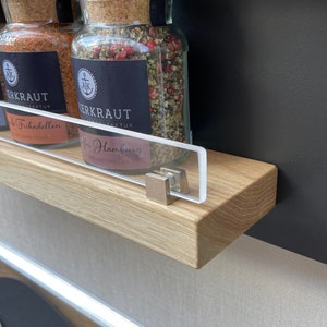 Puede incluir: Tres tarros de especias de vidrio con tapas de corcho y etiquetas negras. Las etiquetas tienen texto blanco que dice "Herbkraft" y el nombre de la especia. Los tarros est&aacute;n sobre una estanter&iacute;a de madera con un frente de acr&iacute;lico transparente.