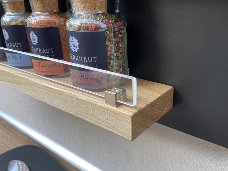 Puede incluir: Tres tarros de especias de vidrio con tapas de corcho y etiquetas negras. Las etiquetas tienen texto blanco que dice "Herbkraft" y el nombre de la especia. Los tarros est&aacute;n sobre una estanter&iacute;a de madera con un frente de acr&iacute;lico transparente.