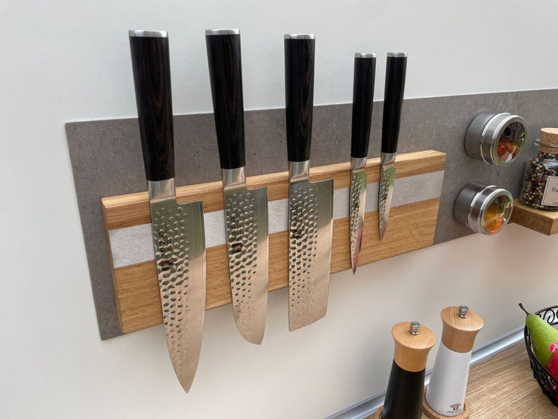 Peut inclure: Un porte-couteaux magn&eacute;tique en bois avec cinq couteaux de cuisine argent&eacute;s attach&eacute;s. Le porte-couteaux est mont&eacute; sur un mur gris avec une bande blanche. Il y a deux petits r&eacute;cipients en argent avec des couvercles sur le mur &agrave; droite du porte-couteaux.