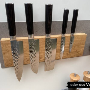 Peut inclure: Un porte-couteaux magn&eacute;tique en bois avec six couteaux attach&eacute;s. Le porte-couteaux est en bois brun clair et a un fond gris. Les couteaux sont de tailles diff&eacute;rentes et ont des manches noirs.
