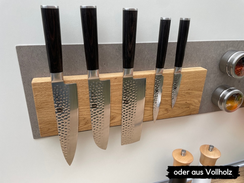 Peut inclure: Un porte-couteaux magn&eacute;tique en bois avec six couteaux attach&eacute;s. Le porte-couteaux est en bois brun clair et a un fond gris. Les couteaux sont de tailles diff&eacute;rentes et ont des manches noirs.