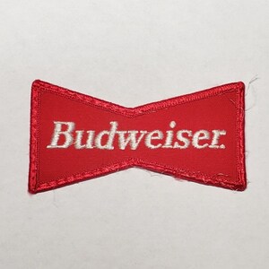 Könnte beinhalten: Roter Stoff-Patch in Form einer Fliege mit weiß gesticktem Text "Budweiser".