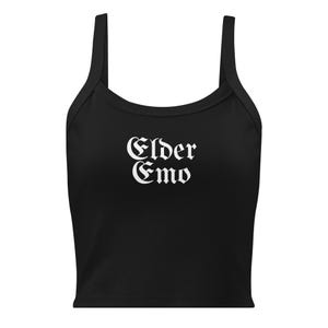 May include: Black crop top with wide straps. The text "Elder Emo" is printed in white gothic lettering across the front. The top is a solid black color.