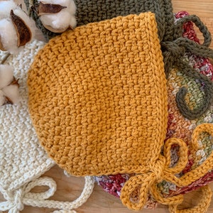 Könnte beinhalten: Drei gehäkelte Baby-Mützen in verschiedenen Farben: Weiß, Senfgelb und ein mehrfarbiger Ombre. Die Mützen sind mit einer einfachen Masche gearbeitet und haben Bänder.