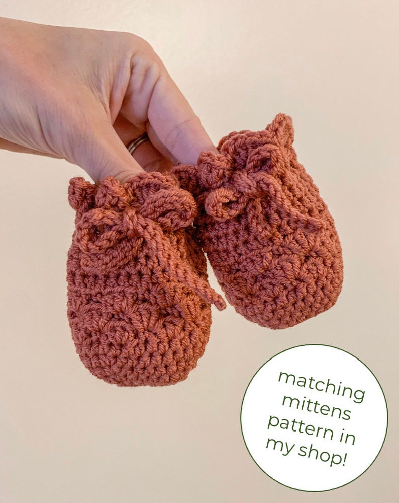May include: A pair of crocheted baby booties in a terracotta color with a bow detail. Matching mittens pattern available in shop.