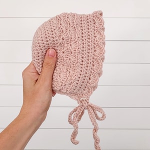 May include: A pink crocheted baby bonnet with a tied bow at the bottom.