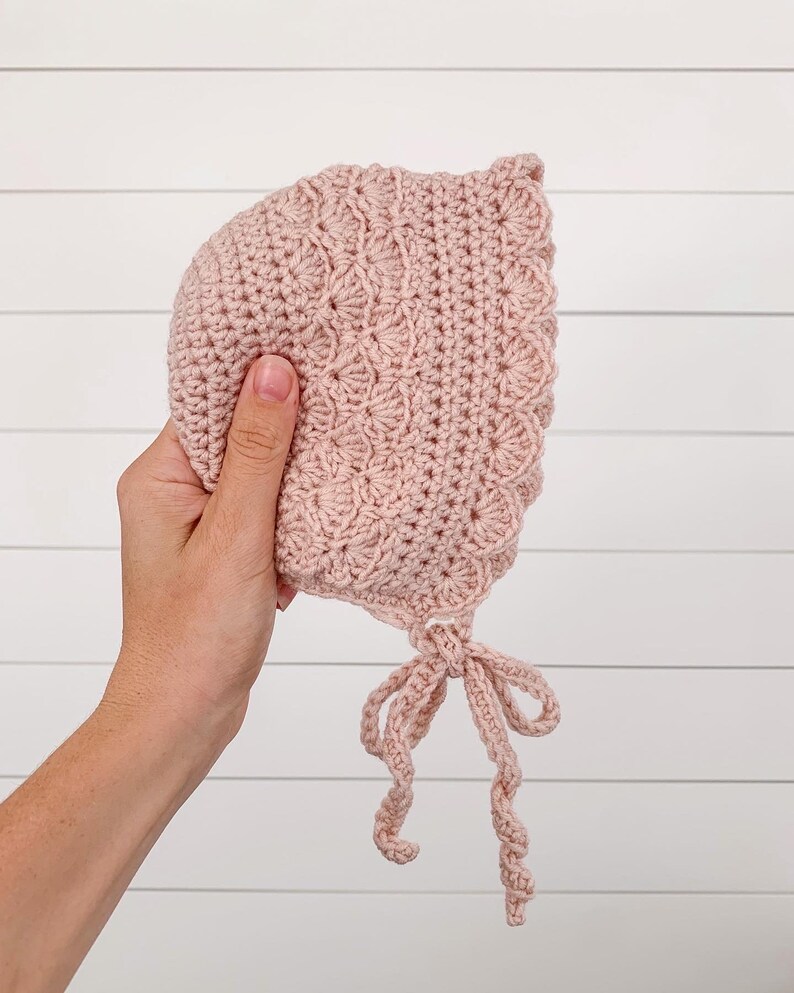 May include: A pink crocheted baby bonnet with a tied bow at the bottom.