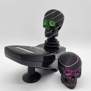 May include: A black joystick with a green and black skull on top and a pink and black skull on the base.