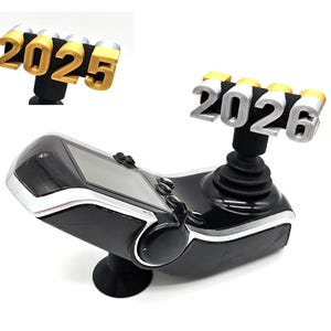 May include: A black and silver joystick with a screen and the numbers 2026 in silver and gold. The joystick has a black base and a silver trim around the screen.