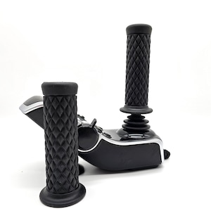 May include: Two black motorcycle grips with a diamond pattern. The grips are attached to a black motorcycle handlebar.