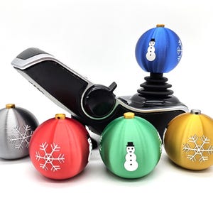 May include: A black joystick with five Christmas baubles attached to it. The baubles are silver, red, green, gold, and blue. Each bauble has a snowflake or snowman design.