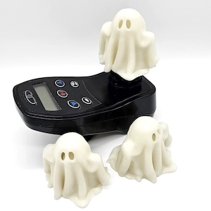 May include: Three white ghost figurines with black eyes. The ghosts are made of a smooth, soft material and are about 10 cm tall. The ghosts are sitting on a black surface.