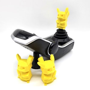 May include: A black joystick with a yellow character figurine on top. Two more yellow character figurines are on the table below the joystick.