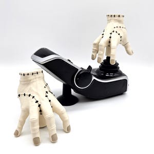 May include: A black and silver joystick with a cream-coloured hand prop. The hand prop has black stitching details. Another hand prop is positioned to the left of the joystick. The background is white.