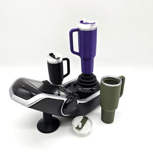 Peut inclure: Divers gobelets isothermes et tasses de voyage de couleurs variées, dont violet, noir et vert olive. Les tasses, avec poignées et couvercles, sont présentées sur une base noire et argentée. L'image est sur fond blanc.
