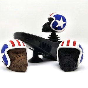 May include: Three black gorilla head figurines wearing red, white and blue helmets. The helmets have a star design. The figurines are on a black base.