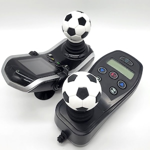 Könnte beinhalten: Zwei schwarze Controller mit einem Fußball auf jedem. Die Controller haben einen Bildschirm und Knöpfe.