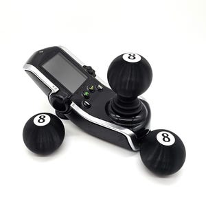 Könnte beinhalten: Ein schwarzer Joystick-Controller mit drei schwarzen Billardkugeln mit weißen Nummer 8 darauf. Die Kugeln sind am Joystick befestigt.