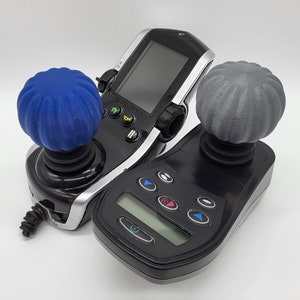 Peut inclure: Deux manettes de jeu noires avec des boutons texturés bleus et gris. Les manettes ont plusieurs boutons et un écran sur l'une des manettes.