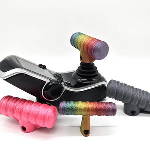 May include: A black and silver joystick with several colorful, textured handles. The handles are in shades of pink, gray, and rainbow. The joystick has a black base and a silver top.