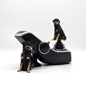 Könnte beinhalten: Eine schwarze und braune Rottweiler-Hundefigur sitzt auf einem schwarzen Joystick mit silbernem Besatz. Eine weitere Rottweiler-Figur sitzt auf der Basis des Joysticks.