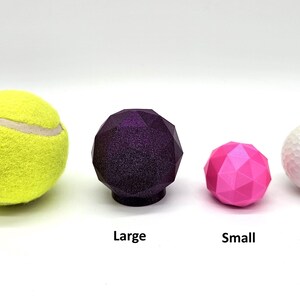 May include: Four different sized balls, a yellow tennis ball, a large purple ball, a small pink ball, and a white golf ball.