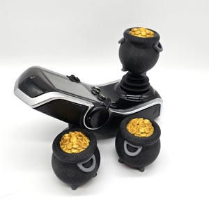 Könnte beinhalten: Ein schwarzer Gaming-Controller mit drei goldenen Topf-mit-Münzen-Toppern. Der Controller hat einen Bildschirm und einen Joystick.