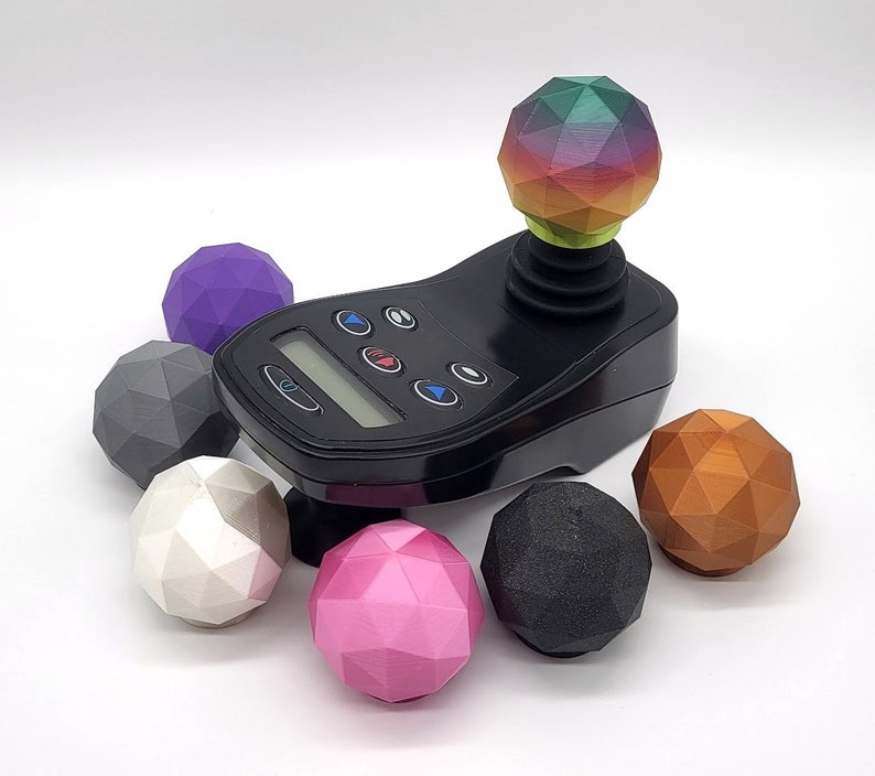 May include: A black joystick with a rainbow-coloured ball on top. There are six different coloured balls surrounding the joystick, including purple, grey, white, pink, black, and copper.