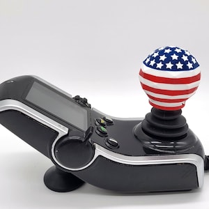 May include: A black joystick controller with a screen and a red, white, and blue American flag-themed ball on top.