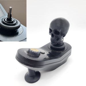 May include: A black joystick with a skull-shaped knob. The joystick has a black base and a black button on the side.