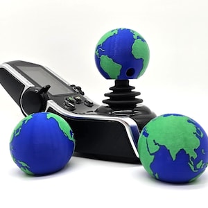May include: A black joystick with a green and blue globe on top. Two more green and blue globes are on the table next to the joystick.