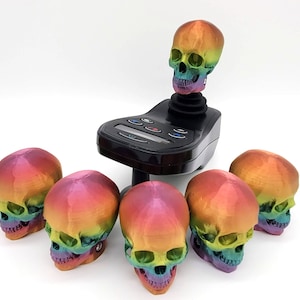 May include: Six rainbow-colored skull-shaped knobs for a joystick. The skulls are made of a smooth, shiny plastic. The joystick base is black and has a control panel with buttons.
