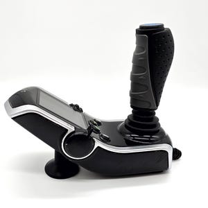 Peut inclure: Un joystick de jeu noir et argent avec une poignée texturée grise et un petit écran sur la base.